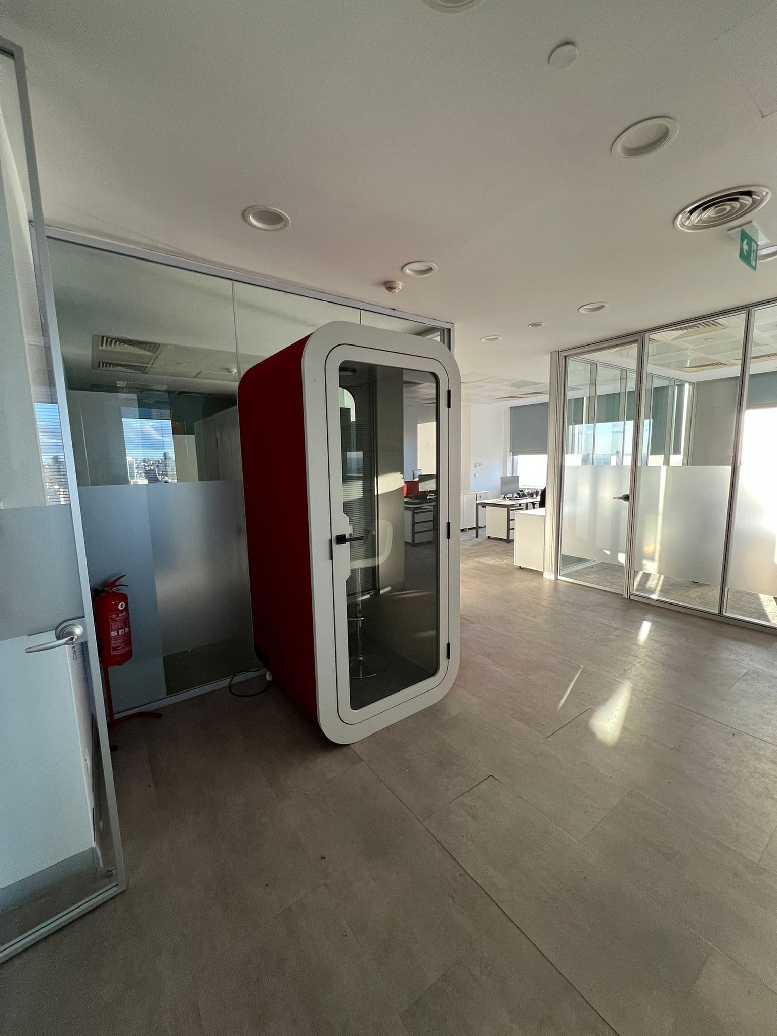 Red one-person booth in a corridor lined with glass-walled offices